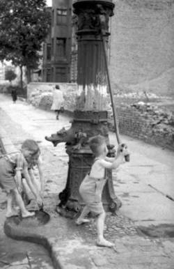 Kinder waschen sich mit einer Wasserpumpe am Rand der Straße.