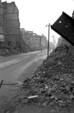 Blick in eine von zerstörten Gebäuden und Trümmerhaufen gesäumte Straße