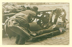 Novemberrevolution: Tote aus Marinehaus; drei Männer bahren einen Toten auf, hinter ihnen links drei weitere Leichen auf einem Wagen