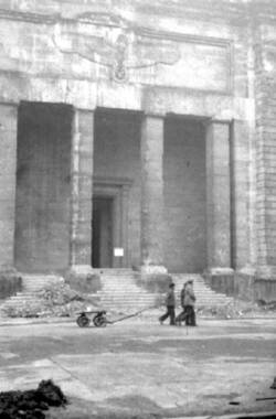 Personen mit Handwagen passieren das Eingangsportal der zerstörten Reichskanzlei
