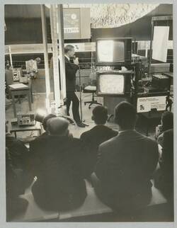 "Gießversuch (Gußeisen) wird mittels Mikroskop und Fernsehkamera auf Bildschirme übertragen". Industrieausstellung Berlin 1968