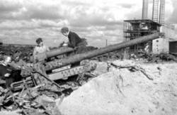 Mehrere Männer suchen Material aus den Weltkriegs-Trümmern, Im Hintergrund ein zerstörtes Fabriksgebäude.