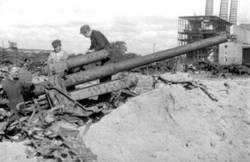 Mehrere Männer suchen Materialien aus den Weltkriegs-Trümmern, Im Hintergrund ein zerstörtes Fabriksgebäude.