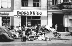 o.T., Straßenszene: Passanten bei einem Müll-Haufen vor einem Tabekwaren- und Lotto-Laden und der Kneipe "Destille"