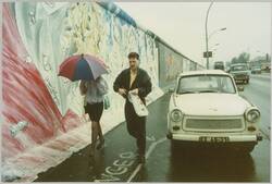 o.T., Fußgänger mit Regenschirm und parkender Trabant neben der Berliner Mauer