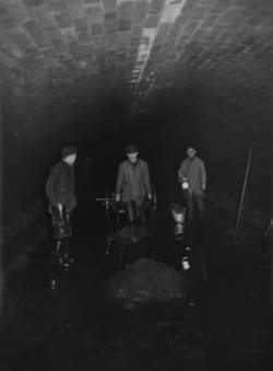 Unter den Straßen von Berlin. Drei Arbeiter im Tunnel mit Schubkarren