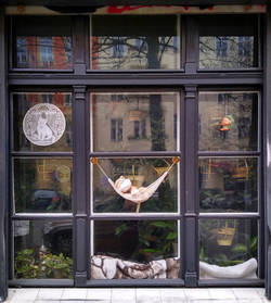 "Geschütztes Abhängen". Fenster einer Parterre-Wohnung mit Dekoration: Plüschtier in Hängematte mit Mundschutz