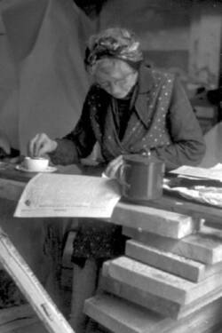 Eine Frau sitzt an einem provisorischen Tisch und tunkt lesend ihr Brot in eine Tasse Kaffee