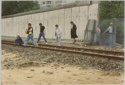 o.T., Personen überqueren in Höhe eines geöffneten Grenzzauns ein Bahngleis